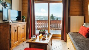 A cozy cabin interior with wooden walls, a dining area with breakfast items, a TV, and a view of a snowy landscape through large windows. - Fitness, swimming pool, balcony, tv, ski locker, 35m², Les Saisies (Les Saisies)