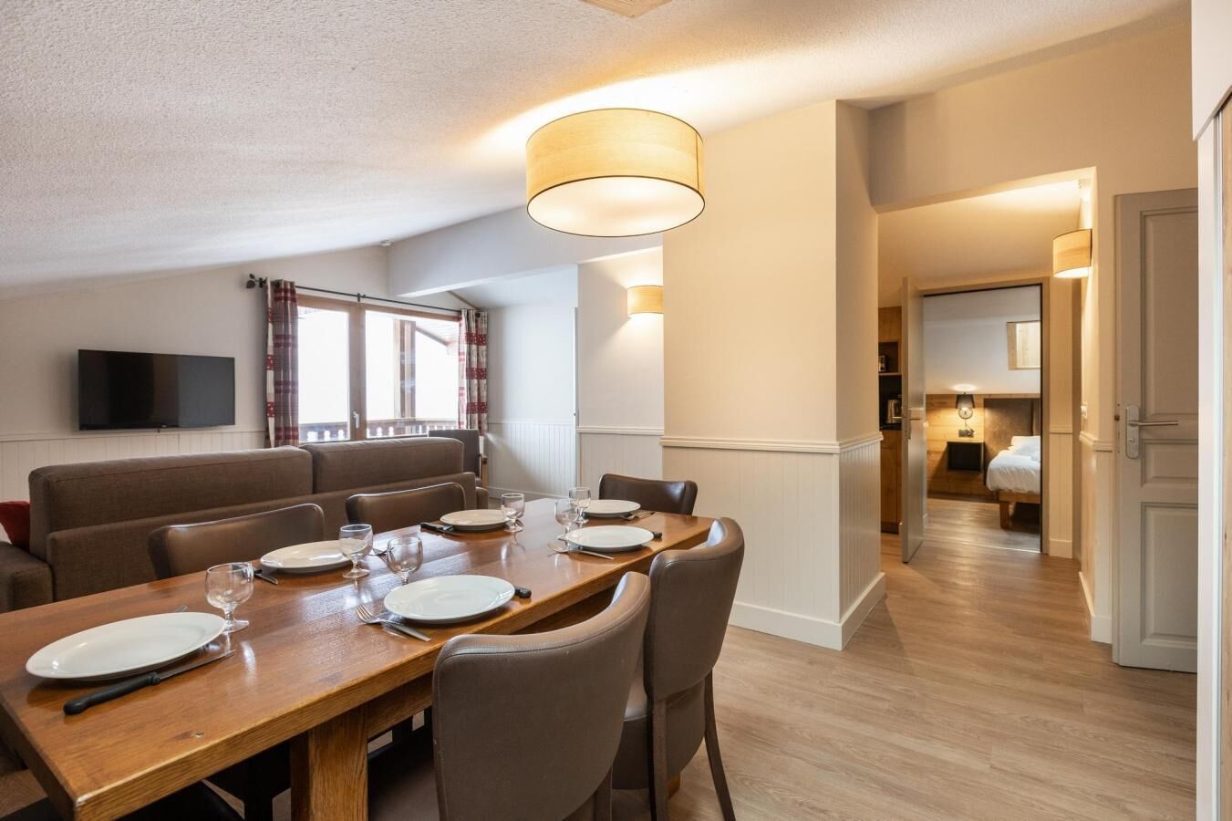 A dining area with a wooden table set for four, a sofa, and a TV mounted on the wall.
