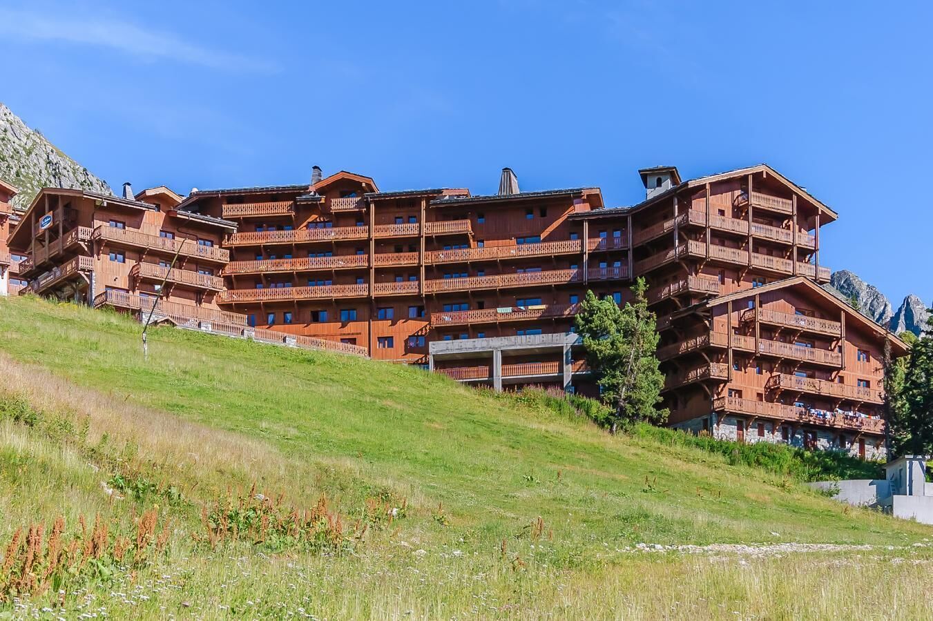 A multi-story wooden hotel with balconies, set on a hillside with a clear sky.