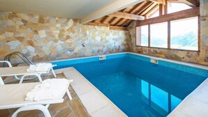 Une piscine intérieure aux murs de pierre, avec une eau d’un bleu cristallin, des poutres en bois et une fenêtre donnant sur un paysage montagneux.