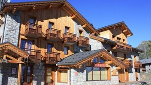 Un bâtiment en bois à plusieurs étages, agrémenté de pierres apparentes, de balcons et d’une enseigne indiquant qu’il s’agit d’un chalet de ski.
