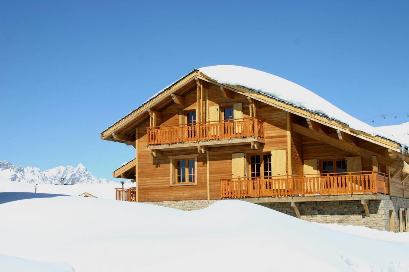 Een houten chalet met een balkon, gelegen tegen een besneeuwde berg.
