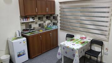 Una cocina compacta con armarios de madera, un refrigerador, un lavamanos y una mesa con mantel floral.