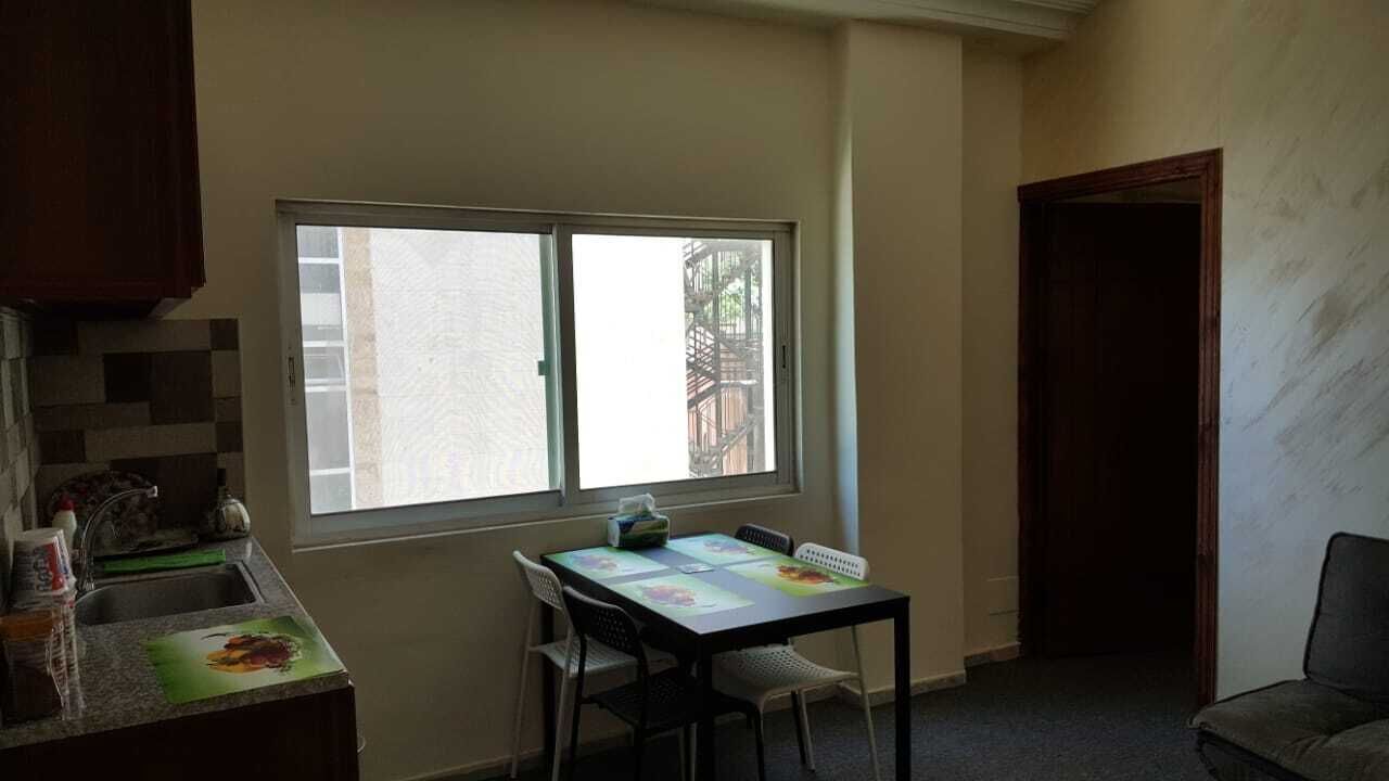 Una pequeña cocina con ventana, una mesa de comedor con sillas y un sofá oscuro.