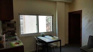 Una pequeña cocina con ventana, una mesa de comedor con sillas y un sofá oscuro.