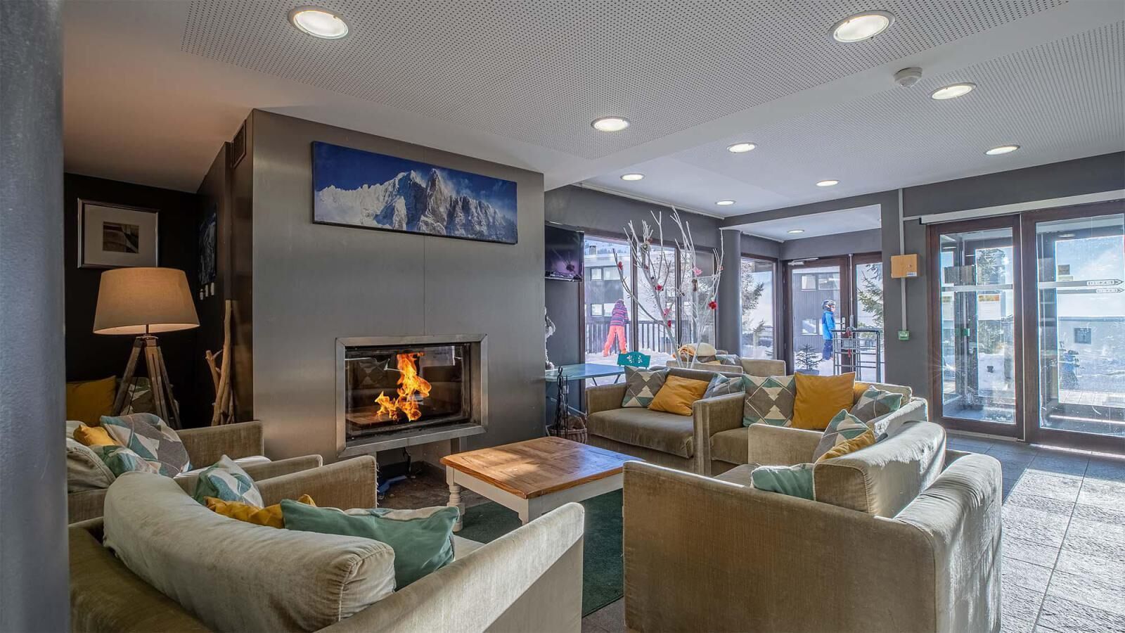 Ein gemütlicher Lounge-Bereich mit Kamin, bequemen Sitzgelegenheiten und großen Fenstern mit Blick nach außen.