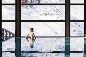 Una persona en traje de baño de pie junto a una ventana con vista a un paisaje nevado.