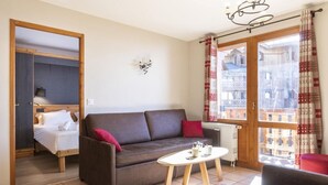 A cozy room with a bed, a sofa, a small table, and a window with curtains. - Wifi, 100m from ski slopes, fitness, swimming pool, sauna, jacuzzi, hammam, balcony, tv, ski locker (Val Thorens)