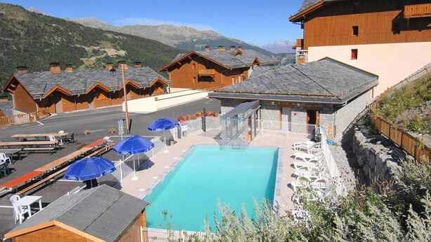 A pool area with lounge chairs and umbrellas, surrounded by wooden buildings with sloped roofs, set against a mountainous backdrop. - Wifi, ski-in/ski-out & foot of the slopes, swimming pool, terrace, balcony, tv, ski locker, 35-40m² (Valmeinier)