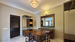 A dining area with a wooden table and chairs, a wall-mounted mirror, and a ceiling light fixture. - King’s Abode - Luxuria Ranakpur by Moustache (Desuri)