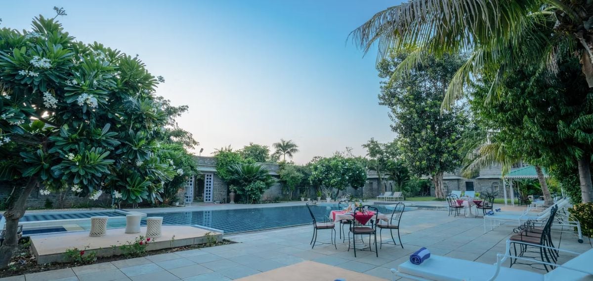 Uma área à beira da piscina com espreguiçadeiras, uma mesa de jantar e um pequeno jardim.