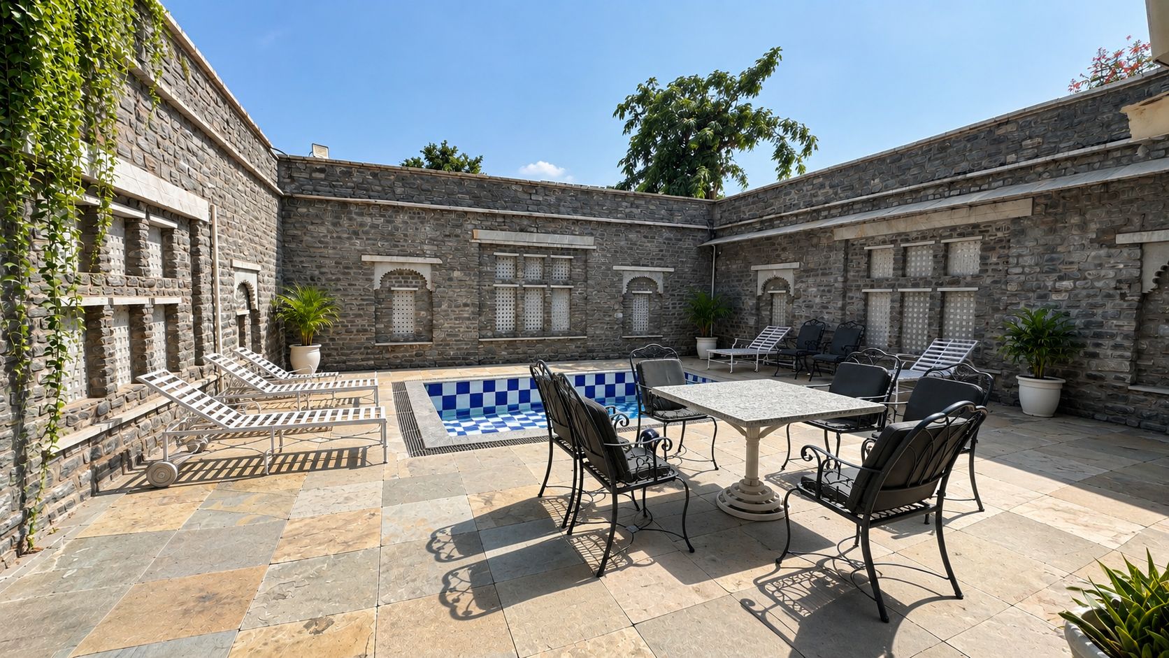 A courtyard with stone walls, a pool with a blue checkered pattern, and outdoor furniture.