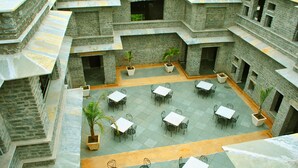 A courtyard with multiple tables and chairs, surrounded by stone walls and potted plants. - King's Abode Ranakpur (Desuri)