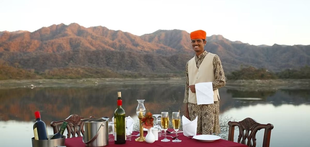 A table set with various bottles and glasses, a person standing beside it, and a mountainous landscape in the background.