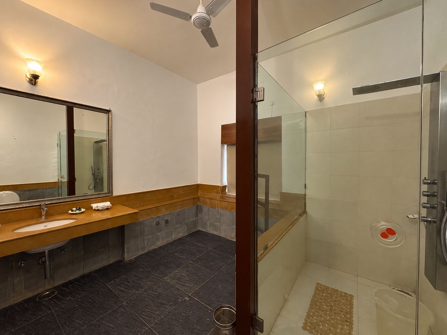 Un baño moderno con ducha envuelta en vidrio, tocador con espejo y ventilador de techo.