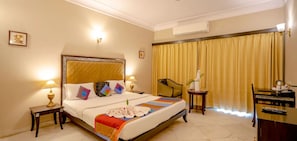 A hotel room with a bed, bedside tables, a chair, a desk, and curtains. - King’s Abode - Luxuria Ranakpur by Moustache (Desuri)