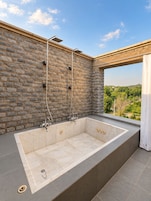 Un baño exterior moderno con pared de piedra, una bañera grande y vistas al campo.