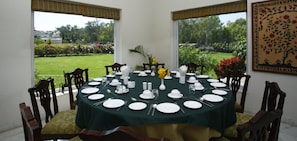Mesa de jantar redonda posta para seis, com pratos brancos, talheres e toalha de mesa verde.