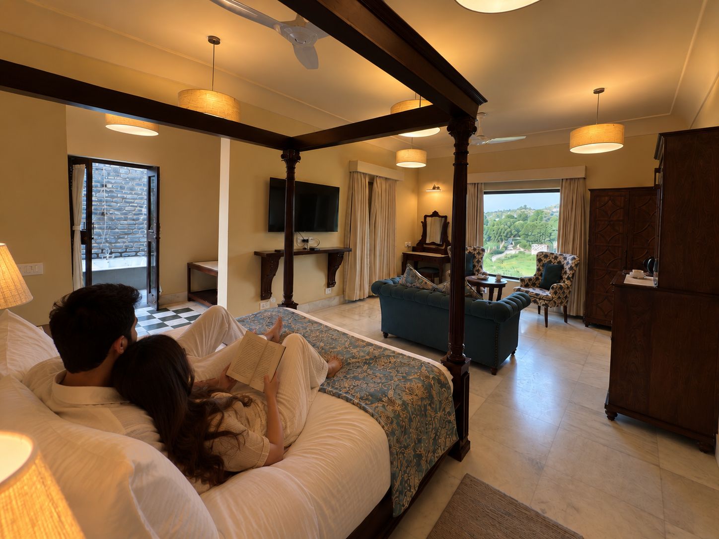 Une chambre à coucher avec un lit à baldaquin, un coin salon avec un canapé et des fauteuils, un téléviseur et une vue sur l’extérieur.