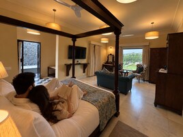 Un dormitorio con cama con dosel, una zona de estar con sofá y sillones, una televisión y vistas al exterior.