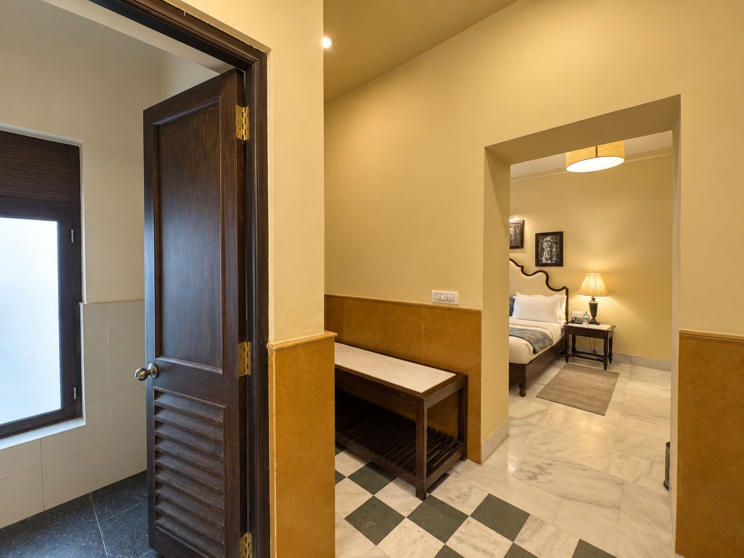 Habitación de hotel con cama, mesita de noche, lámpara y piso a cuadros.