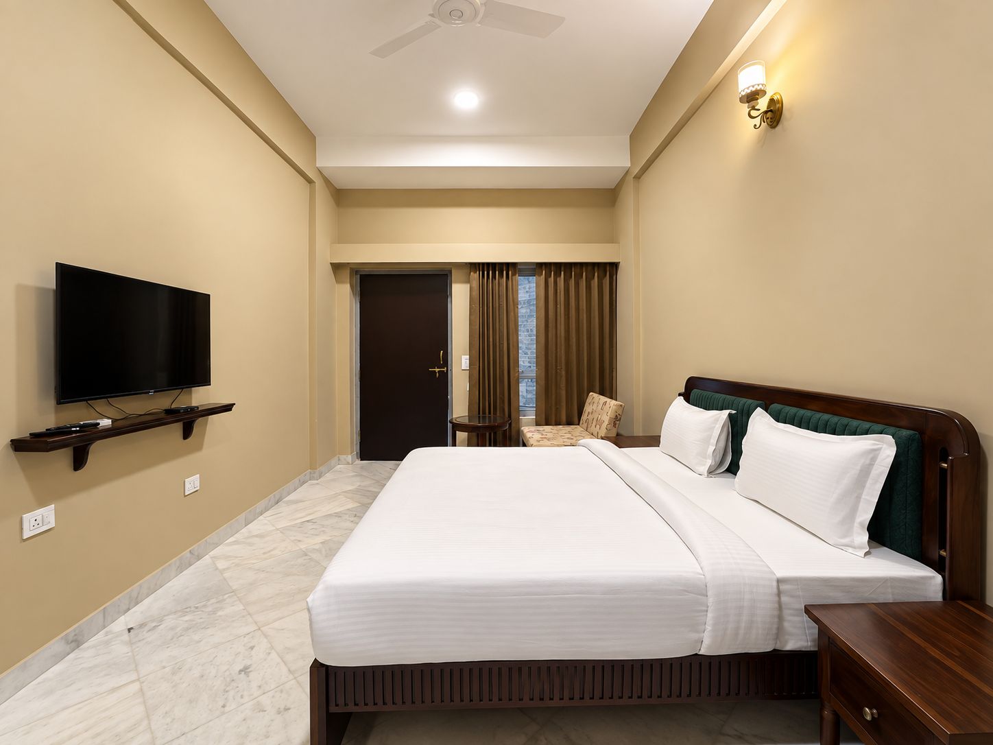 A hotel room with a bed, a television on a stand, a nightstand, and a door leading to a balcony.