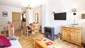 A cozy living room with a wooden dining table, chairs, a sofa, a TV, a fireplace, and a wooden cabinet. - Chalet, wifi, swimming pool, terrace, balcony, tv, ski locker, 45m², Valmeinier (Valmeinier)