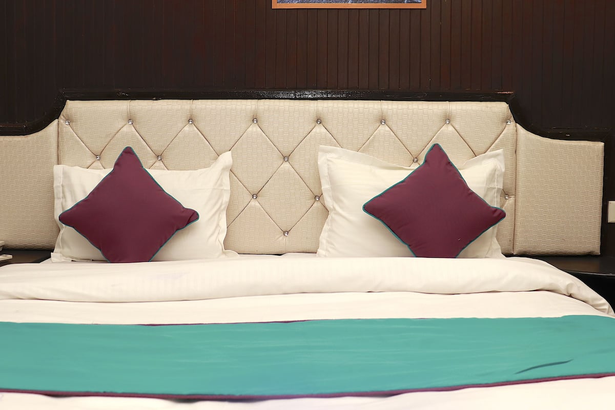 A hotel room with a tufted headboard, two pillows, a bed with a teal and white bedspread, and a bedside telephone.