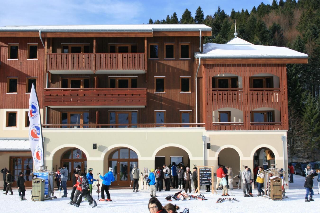 Een meerlaags gebouw met balkons en boogvormige deuropeningen, omringd door mensen en ski-uitrusting.