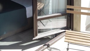Habitación de hotel con cama, un banco de madera y un ventanal que ofrece vistas de la ciudad.
