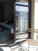 Habitación de hotel con cama, un banco de madera y un ventanal que ofrece vistas de la ciudad.