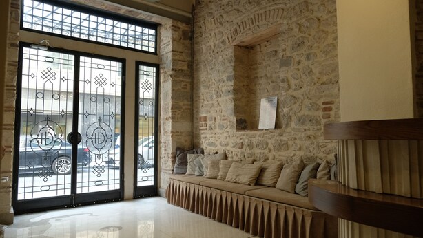 Un vestíbulo con pared de piedra, un banco con cojines y una puerta de cristal grande con barrotes de metal.