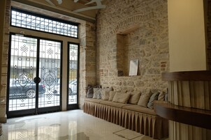 Un vestíbulo con pared de piedra, un banco con cojines y una puerta de cristal grande con barrotes de metal.