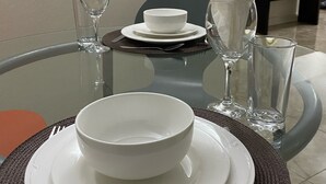 A dining table set with white plates, bowls, and glasses, with a vase of white flowers and a mirror on the wall. - Avisa Stays. A hidden gem. Luxury beach living.  (Ocho Rios)
