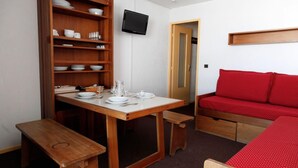 Ein gemütlicher Raum mit Holztisch, gedecktem Esstisch, einem roten Sofa und einem Fernseher an der Wand.