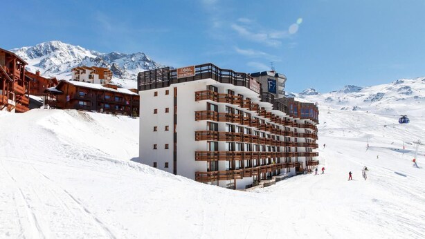 Ein modernes Hotel mit mehreren Etagen, dahinter Skilifte und eine gebirgige Landschaft.