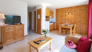 Un ambiente compatto con televisore, mobili in legno, un tavolo da pranzo e angolo cottura.