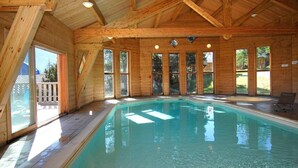 Una baita di legno con una piscina interna ampia, grandi finestre e una zona relax con terrazza.