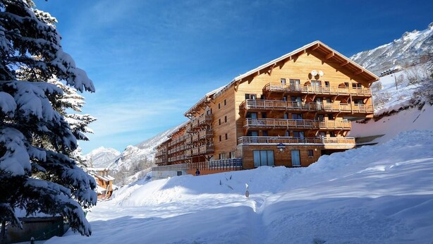 A wooden multi-story building with balconies, surrounded by snow-covered mountains and trees. - Fitness, swimming pool, tv, ski locker, 23m², Vars (Vars)