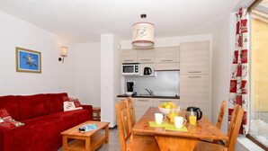A compact living space with a red sofa, wooden dining table, and a kitchenette in the background. - Fitness, swimming pool, tv, ski locker, 23m², Vars (Vars)