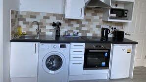 A compact kitchen with a washing machine, microwave, and a small oven. - Pretty Properties Grange House Apartment 2 (Darlington)