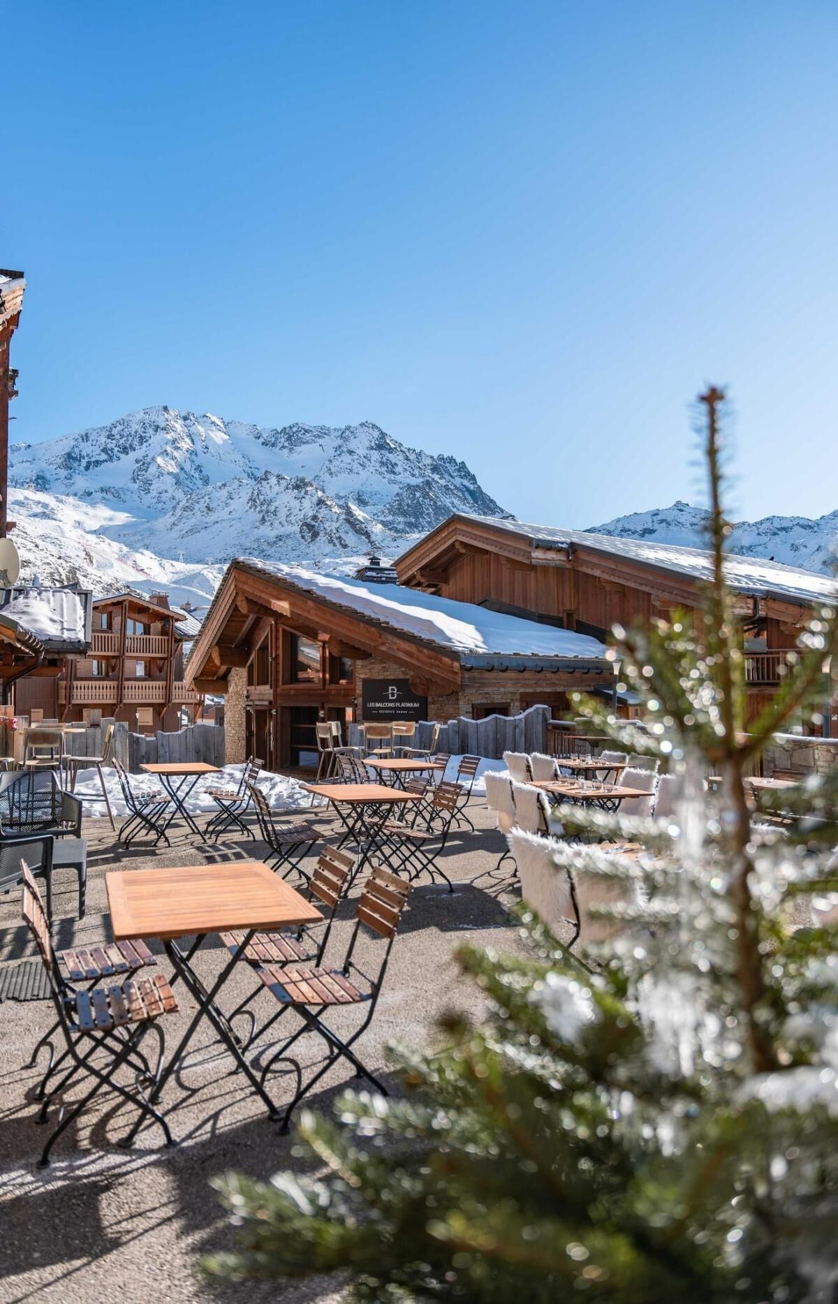 A wooden chalet with outdoor seating and a mountain backdrop.