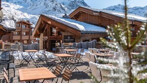 A wooden chalet with outdoor seating and a mountain backdrop. - Wifi, 100m from ski slopes, fitness, swimming pool, sauna, hammam, balcony, fireplace or stove, tv (Val Thorens)