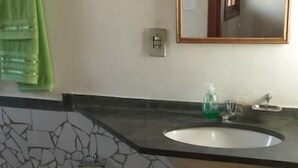 Un baño con piso de mosaico, un lavamanos con espejo y una toalla verde colgada en la pared.
