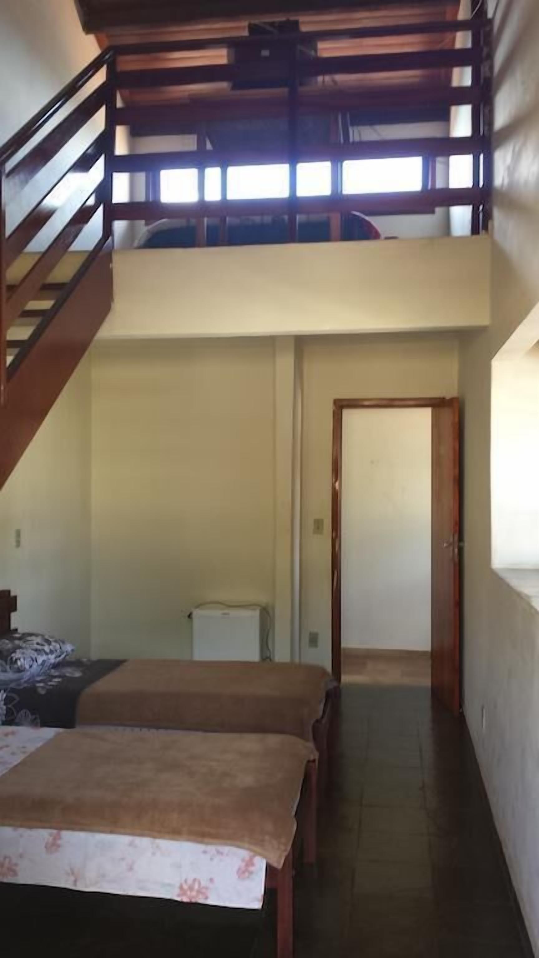 A room with a bunk bed, a small table, and a radiator. There is a staircase leading to an upper level.