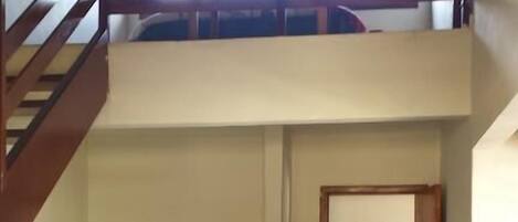 A room with a bunk bed, a small table, and a radiator. There is a staircase leading to an upper level.