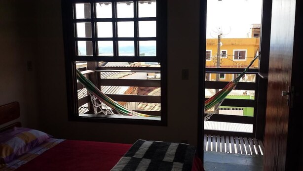 Una habitación con cama, ventana con vista a un edificio y una hamaca afuera.