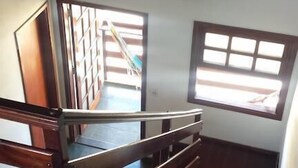 Una escalera de madera que sube a un rellano con vista a un balcón.