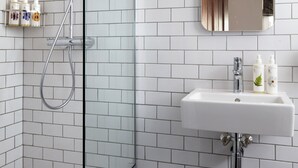 A modern bathroom with white subway tiles, a glass-enclosed shower, a white sink, and a mirror above it. - The Hero of Maida (London)