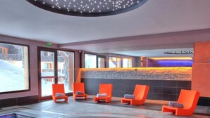 Een moderne binnenzwembadruimte met een stenen muur en oranje stoelen.